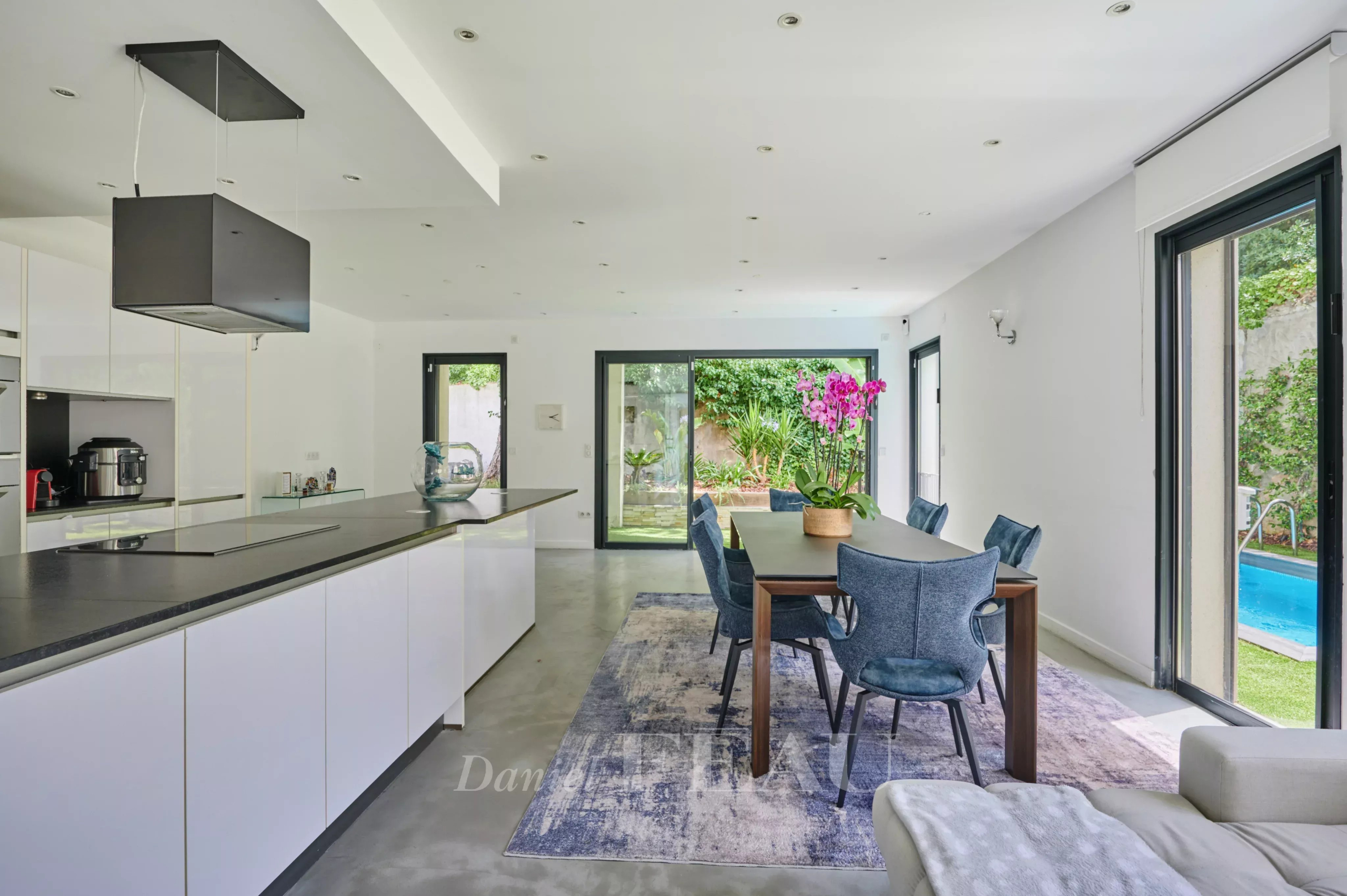 Intérieur d'une maison contemporaine avec cuisine ouverte et salle à manger, vue sur le jardin et la piscine.