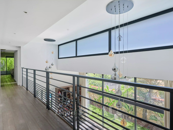 Intérieur d'une maison contemporaine avec balustrade et fenêtres laissant passer la lumière.