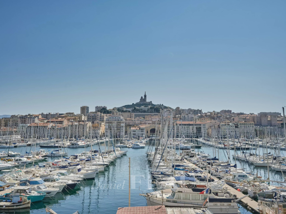 Vue panoramique du Vieux-Port de Marseille avec des bateaux à quai et la basilique Notre-Dame de la Garde en arrière-plan.