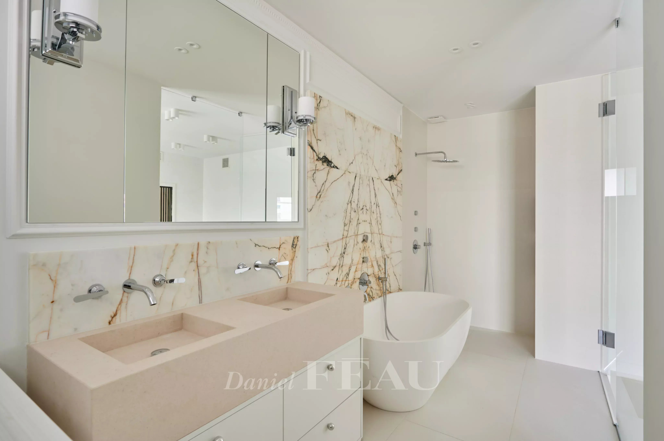 Salle de bain moderne avec baignoire, double vasque et murs en marbre.