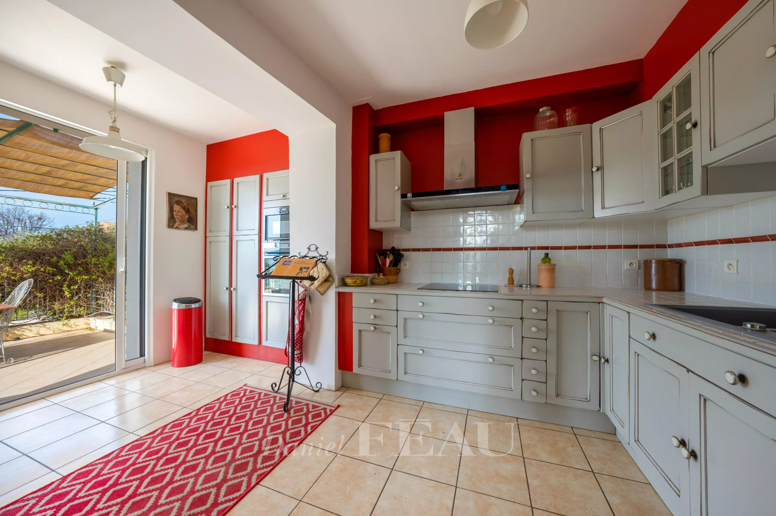 Cuisine moderne avec éléments gris et rouge, accès à une terrasse extérieure.