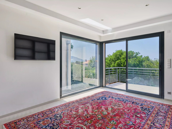 Intérieur lumineux d'une maison avec un tapis persan et de grandes fenêtres donnant sur l'extérieur.