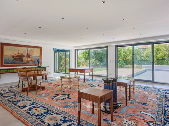 Intérieur d'une maison spacieuse avec un grand salon, des fenêtres donnant sur le jardin et un tapis coloré.