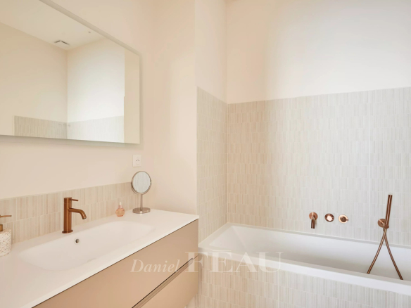 Salle de bain moderne avec baignoire et meuble vasque, murs clairs et robinetterie en bronze.