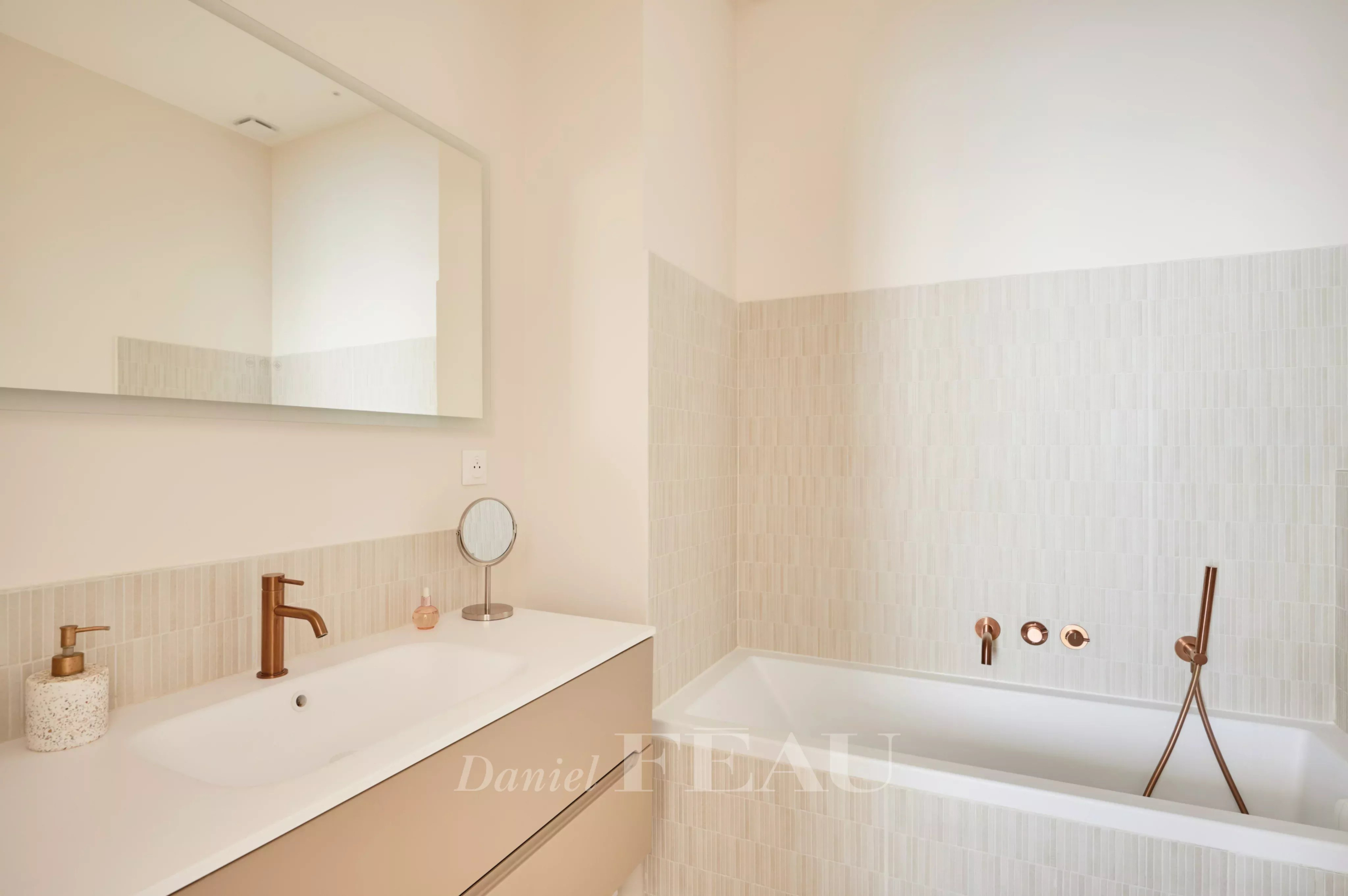 Salle de bain rénovée Salle de bain moderne avec baignoire et meuble vasque, murs clairs et robinetterie en bronze.