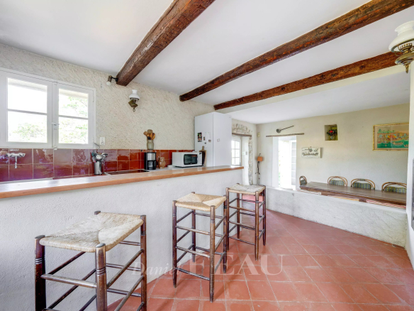 Intérieur d'une bastide en pierres avec bar et chaises en bois, murs clairs et poutres apparentes.