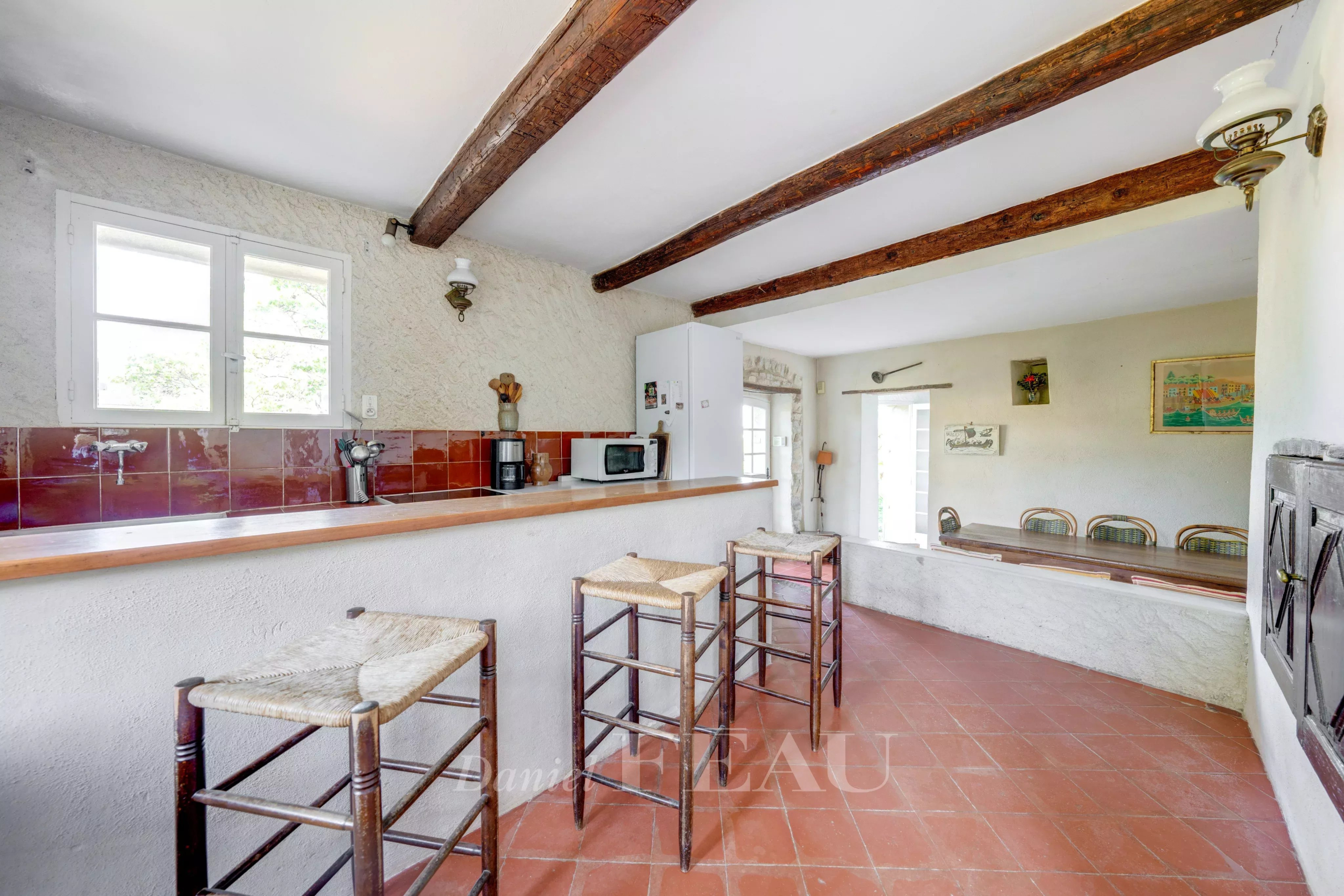 Intérieur d’une bastide au Beausset Intérieur d'une bastide en pierres avec bar et chaises en bois, murs clairs et poutres apparentes.