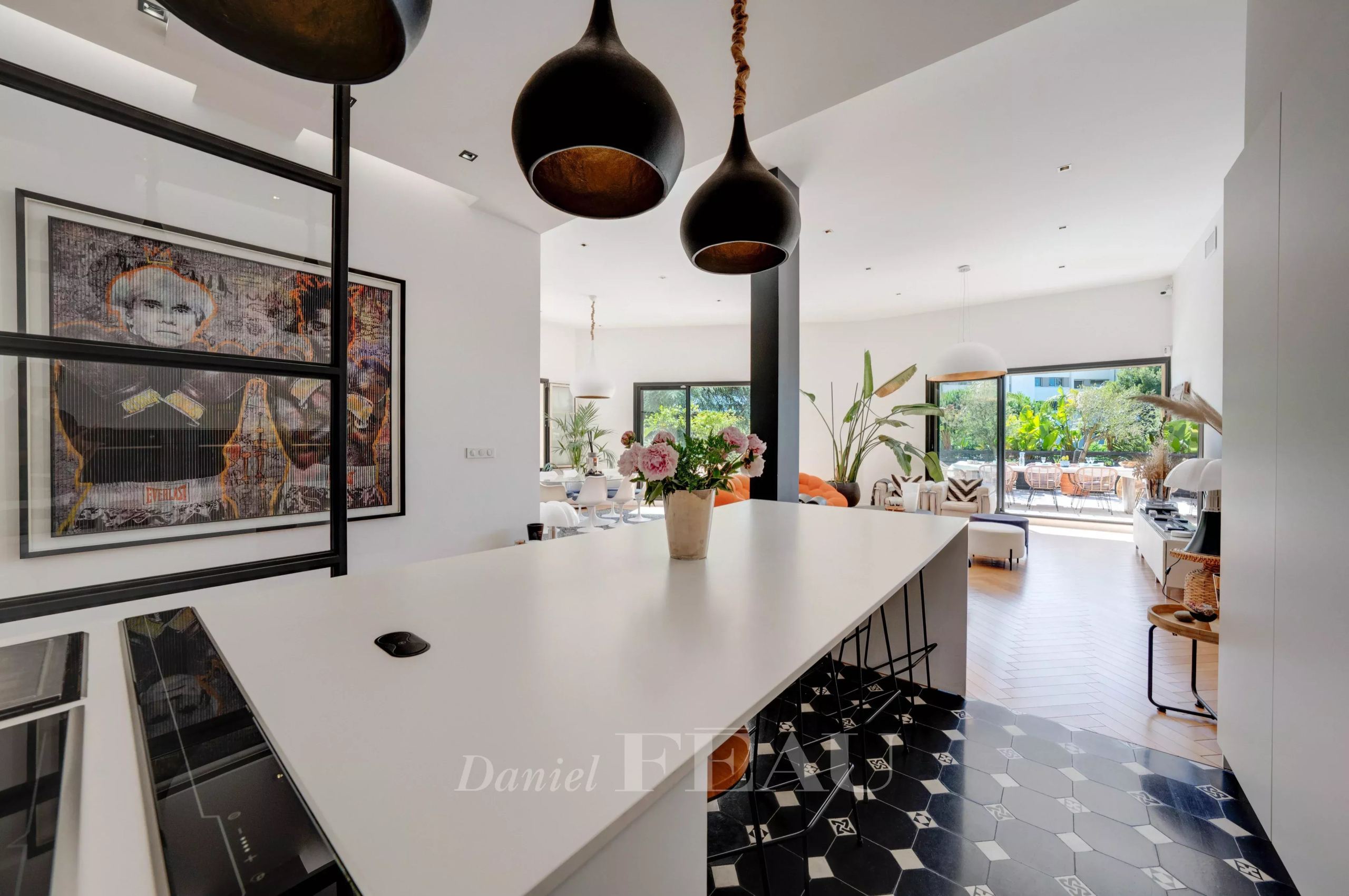 Intérieur d'un appartement moderne avec cuisine ouverte et îlot central, décoré de plantes et d'œuvres d'art.