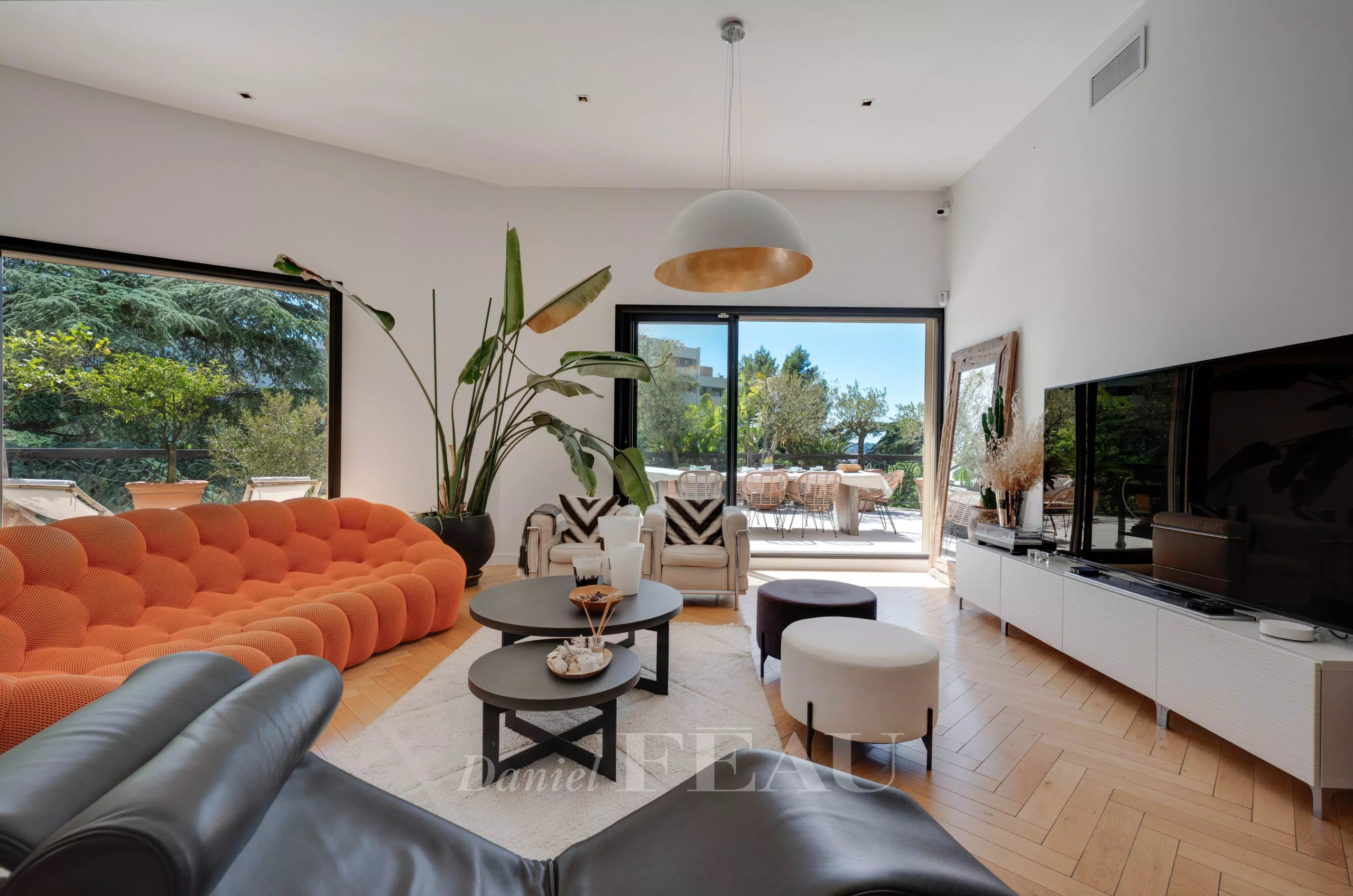 Salon lumineux d'un appartement avec canapé orange et vue sur une terrasse.