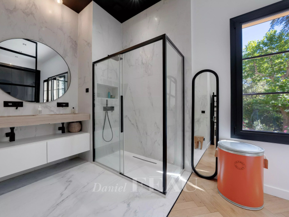 Salle de bain moderne avec douche à l'italienne et miroir rond, lumière naturelle à travers la fenêtre.