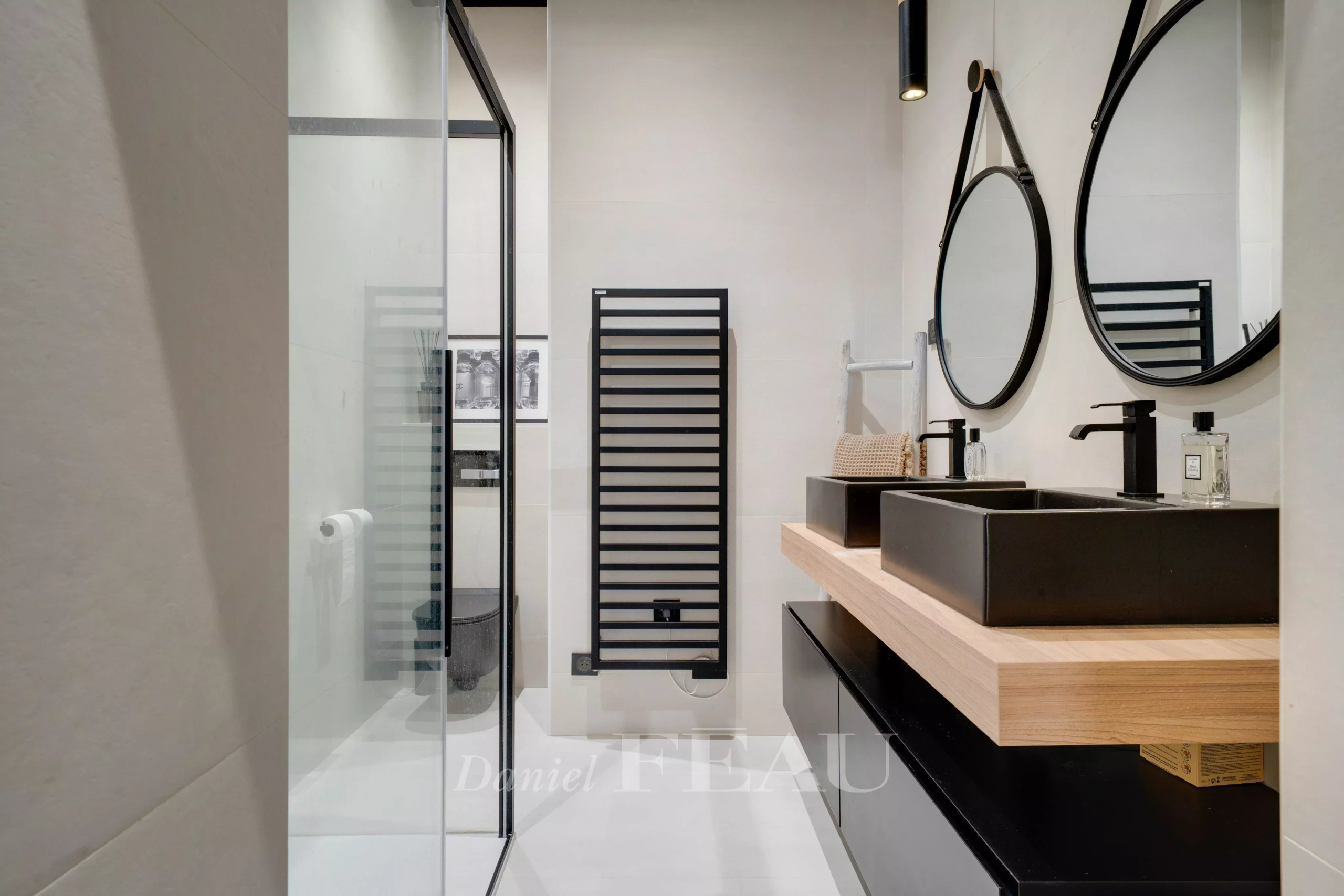 Salle de bain moderne avec douche, double vasque et miroir rond.