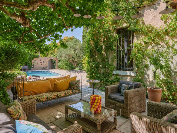 Shaded terrace with garden furniture and swimming pool, surrounded by greenery.