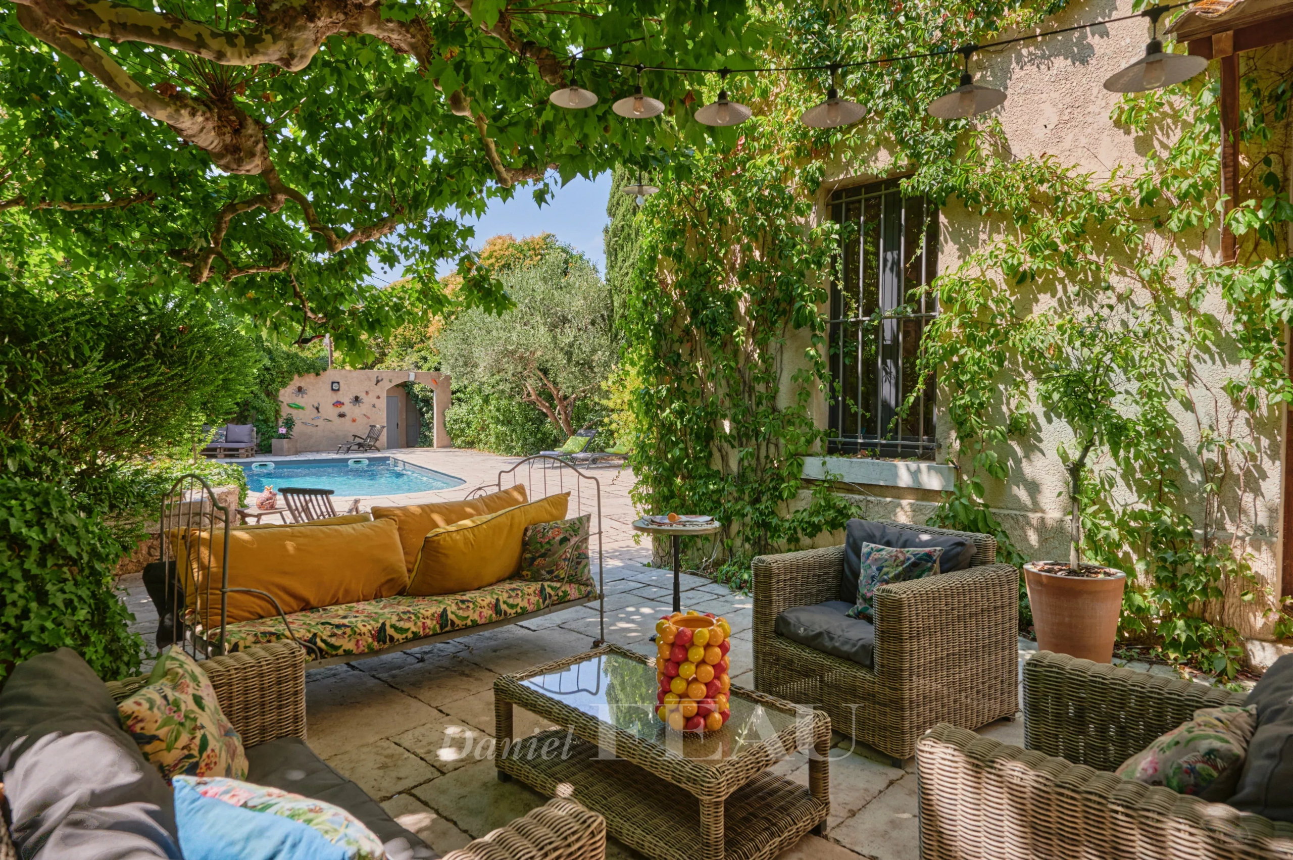 Charming house in Marseille Shaded terrace with garden furniture and swimming pool, surrounded by greenery.