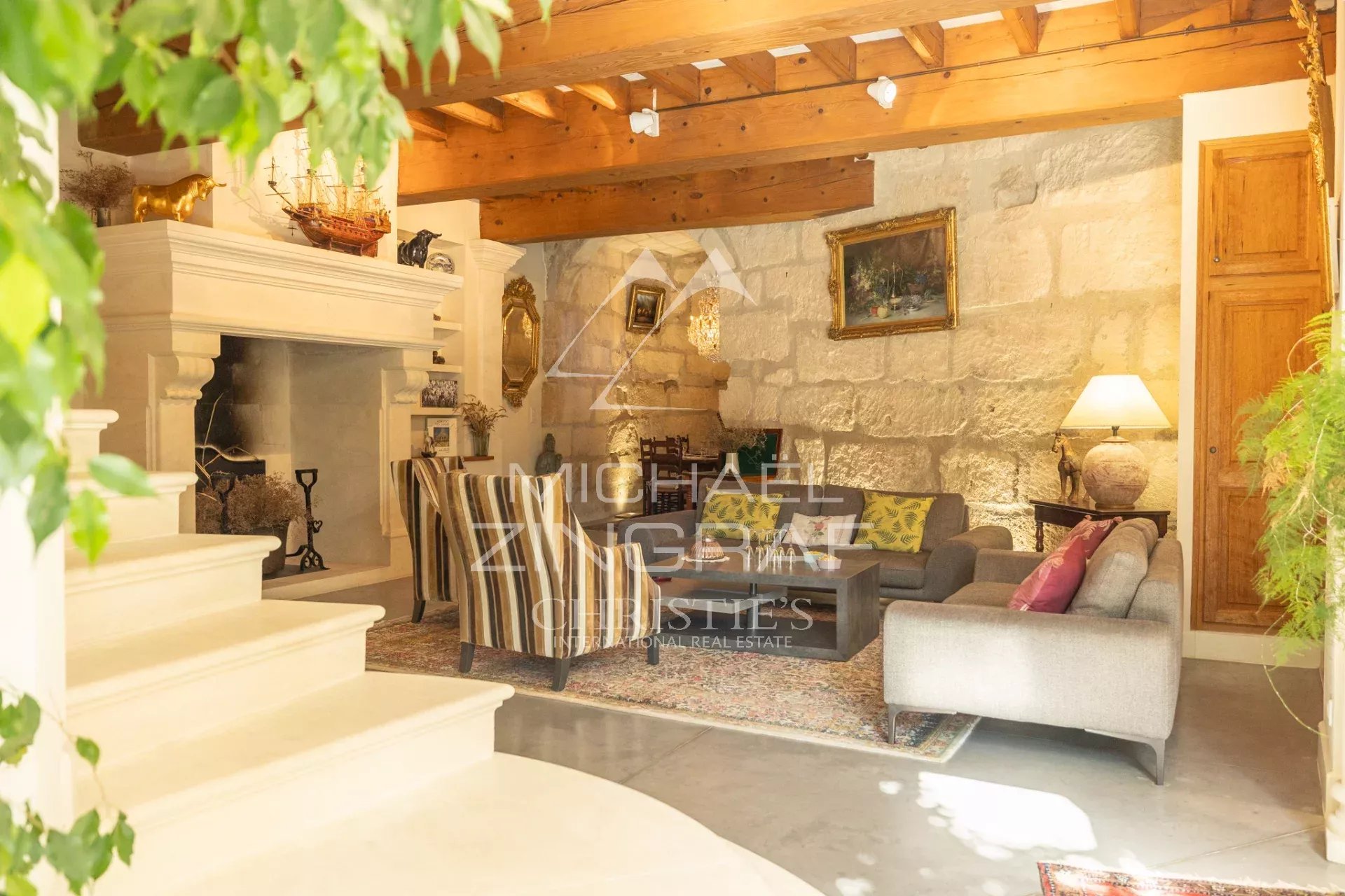 Rustic living room with a large white fireplace, exposed wooden beams, and a seating area with striped chairs.