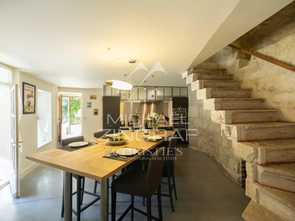 Open-plan kitchen and dining area with a wooden table, stone-wall staircase on the right, and stainless steel kitchen in the background.