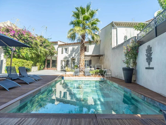 Poolside backyard with a rectangular pool, wooden deck, palm tree, and blue lounge chairs under a sunny sky.