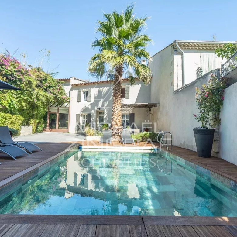 Poolside backyard with a rectangular pool, wooden deck, palm tree, and blue lounge chairs under a sunny sky.