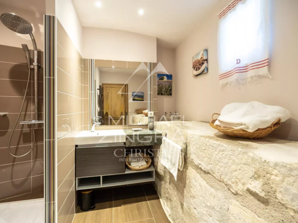 Modern bathroom with a glass-walled shower, a floating vanity sink, and a rough stone counter stacked with towels.