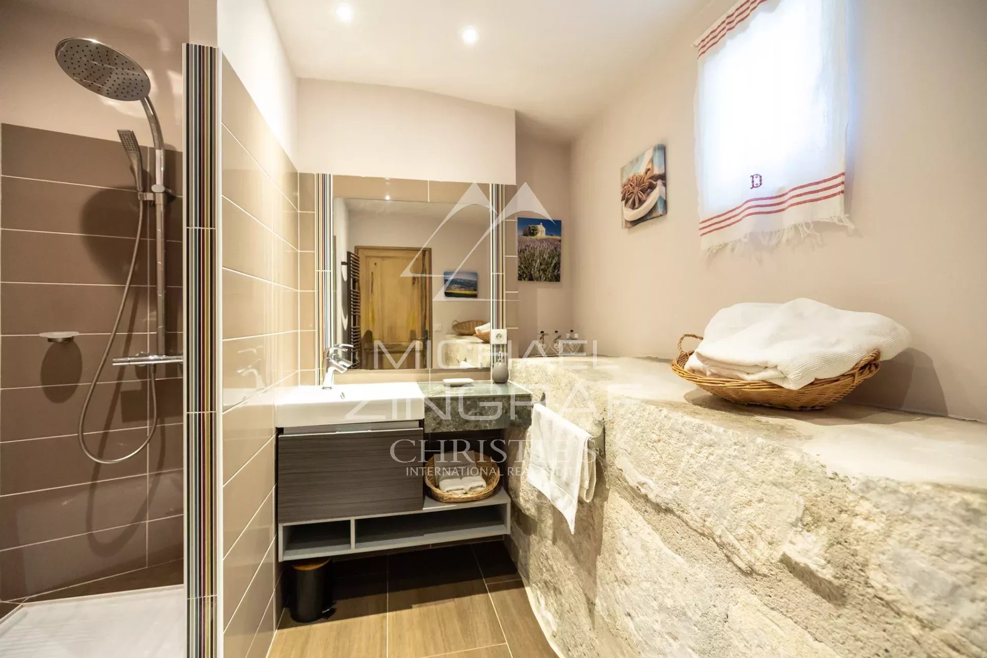 Modern bathroom with a glass-walled shower, a floating vanity sink, and a rough stone counter stacked with towels.