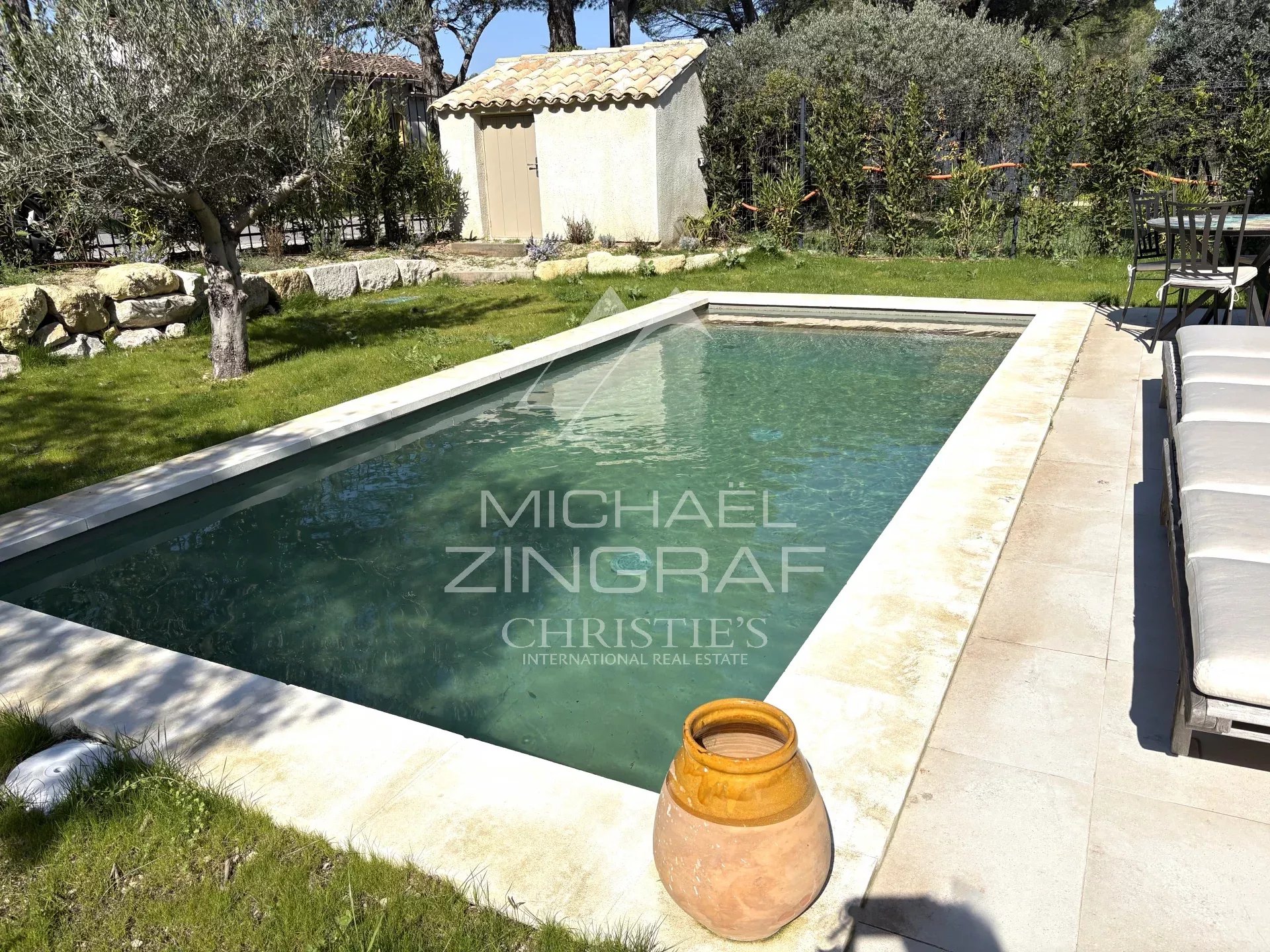Rectangular in-ground pool in a sunny backyard with lounge chairs along the deck and a small shed in the background.