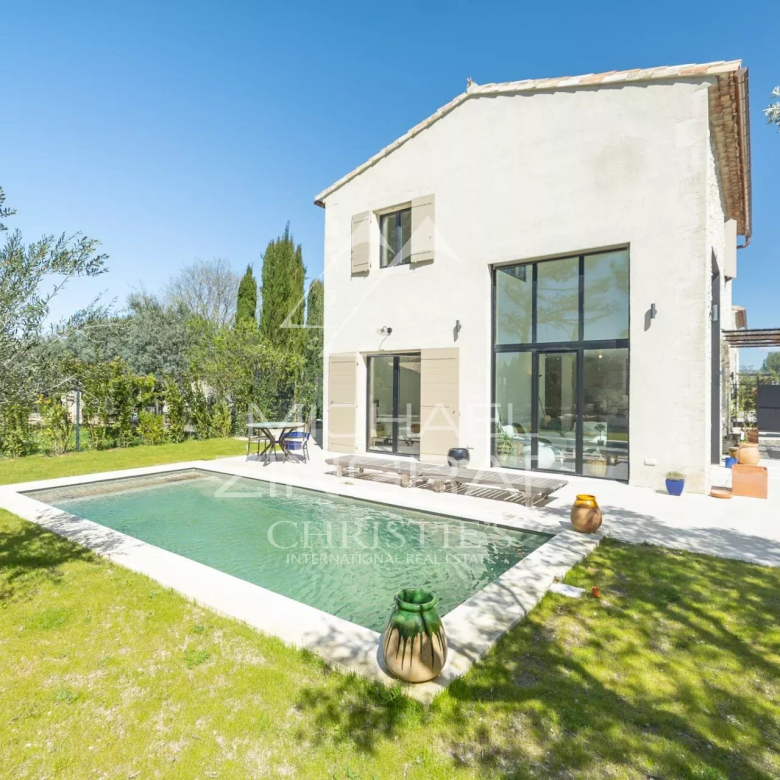 Modern white two-story villa with large glass doors, swimming pool, and green yard on a sunny day.
