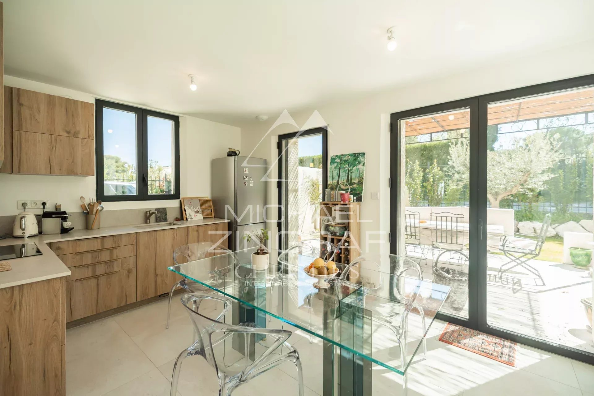 Modern kitchen with wood cabinets, glass dining table, and large sliding doors to a sunny patio.