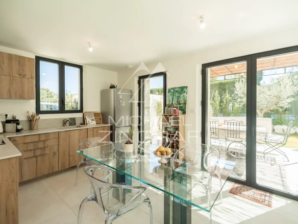 Modern kitchen with glass table and large bay windows overlooking the outside.