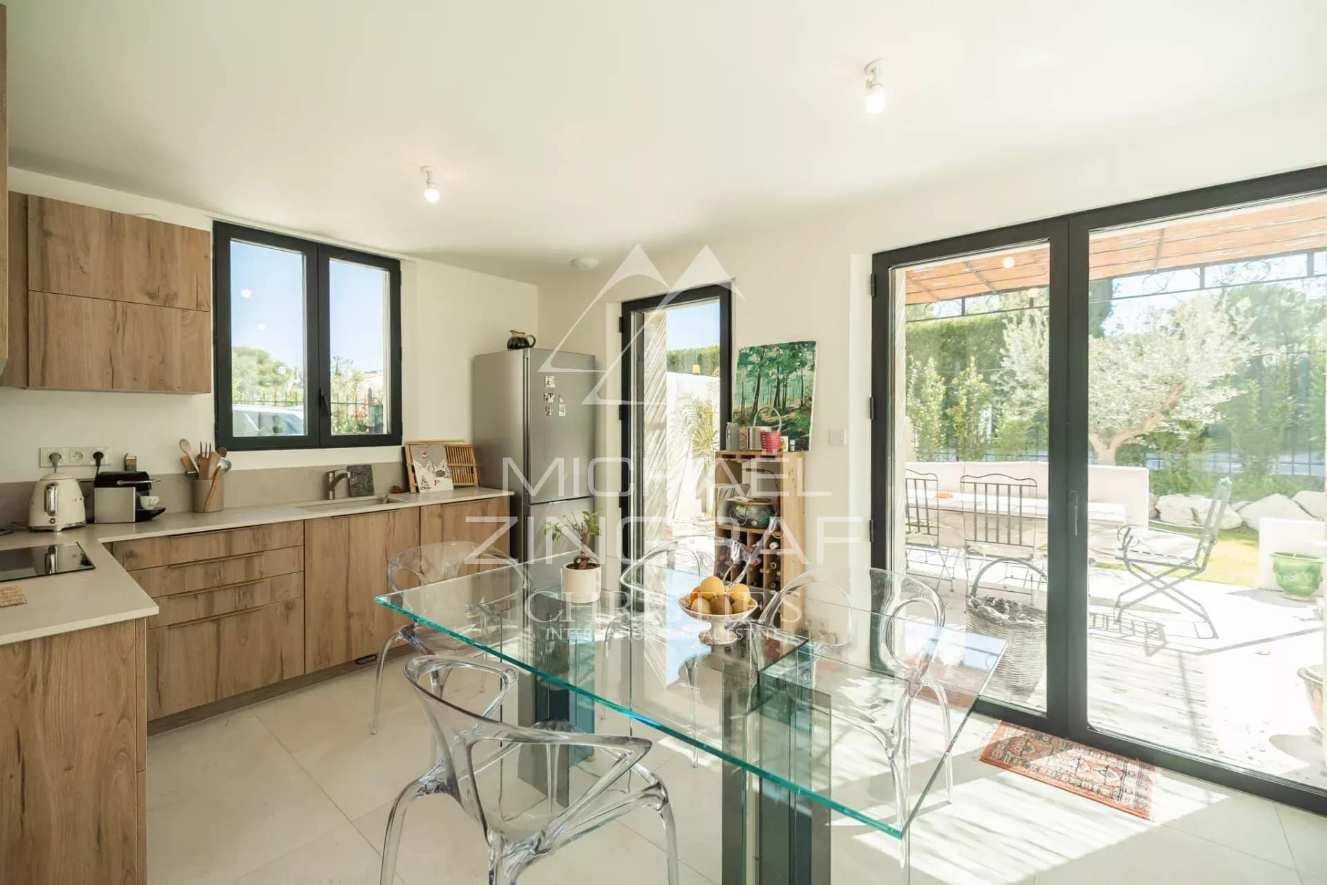 Modern kitchen with glass table and large bay windows overlooking the outside.