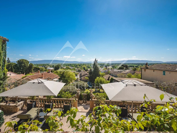 Vue panoramique sur les monts du Luberon depuis une terrasse avec parasols.