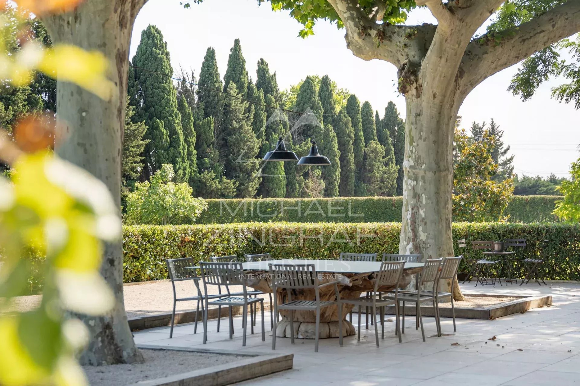 Terrasse du mas rénové à Eyragues Terrasse d'un mas rénové avec table et chaises, entourée d'arbres et de verdure à Eyragues.
