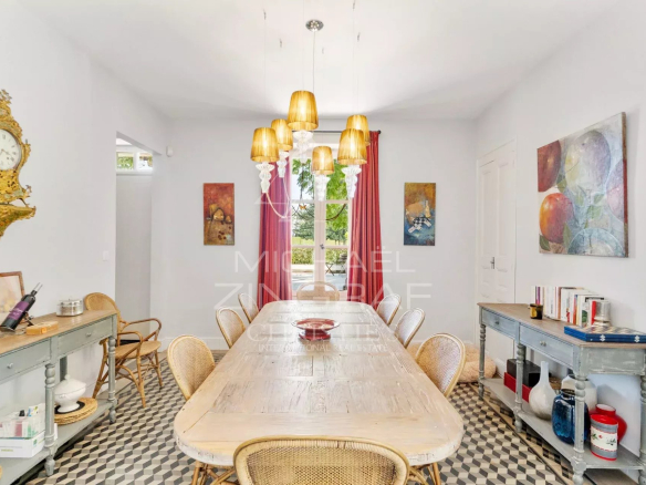 Salle à manger d'un mas rénové avec table en bois et chaises en rotin, décorée de tableaux.