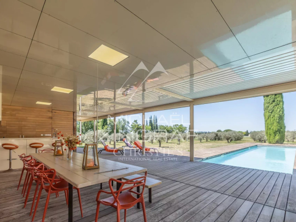 Wooden terrace with table and chairs, overlooking the pool and Provençal landscape.