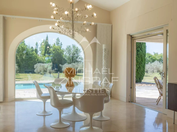 Bright interior of a contemporary house with a dining table and white chairs, overlooking the garden.