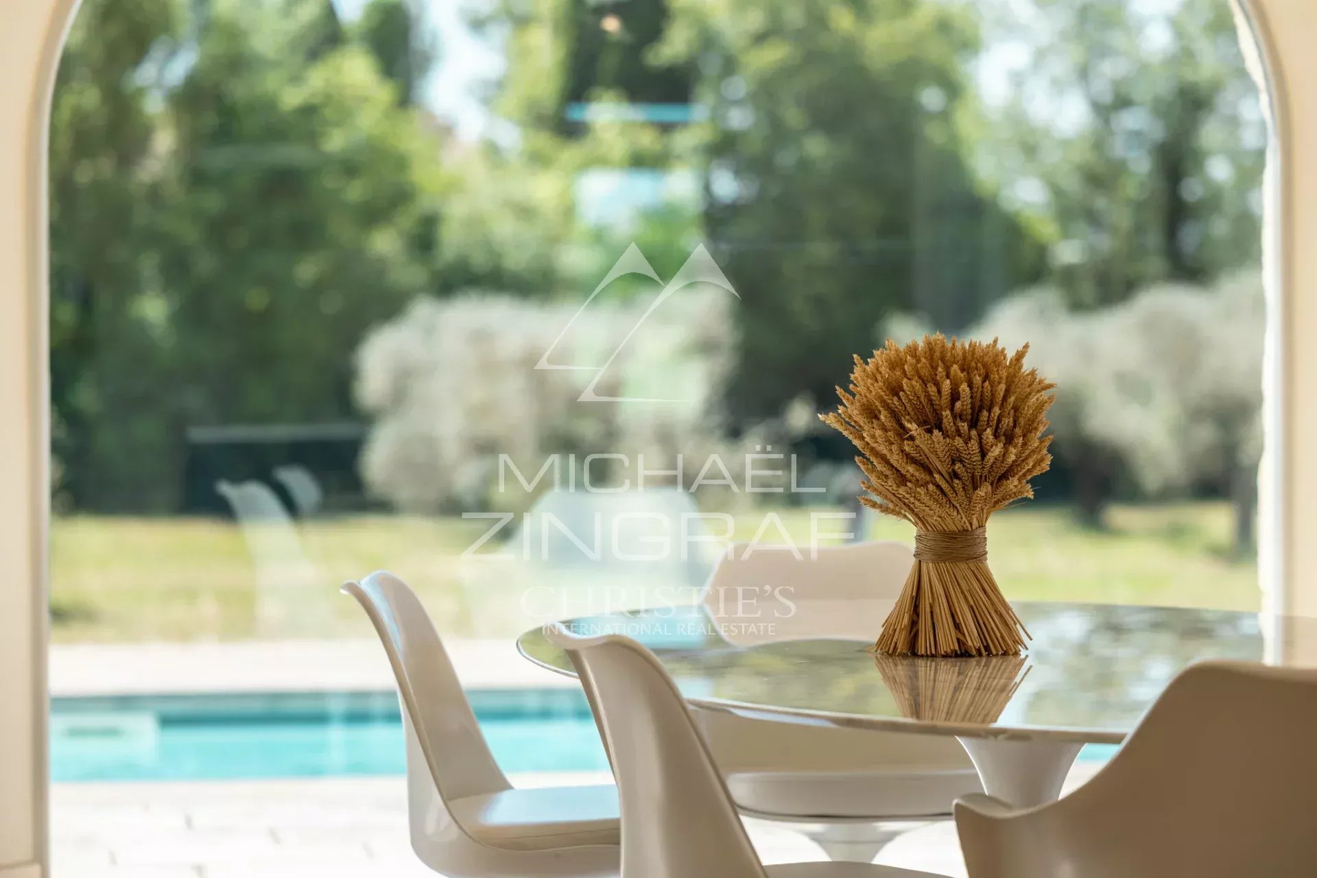 Bright interior with garden view Modern table with a bouquet of wheat in a bright house, overlooking a garden with a swimming pool.