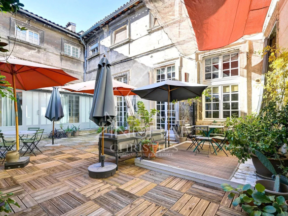 Terrasse ensoleillée d'un hôtel particulier du XVIIème siècle à Avignon, avec parasols et mobilier de jardin.