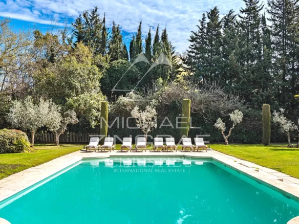 Swimming pool surrounded by greenery in a park, with sun loungers by the water.