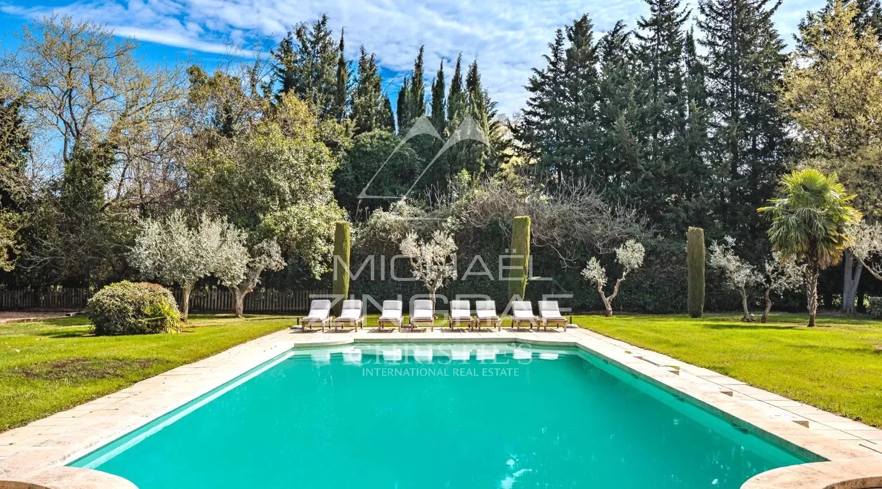 Swimming pool surrounded by greenery in a park, with sun loungers by the water.