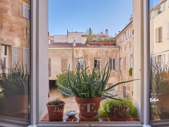 Vue depuis une fenêtre d'un appartement à Aix-en-Provence avec des plantes en pot et des bâtiments anciens en arrière-plan.