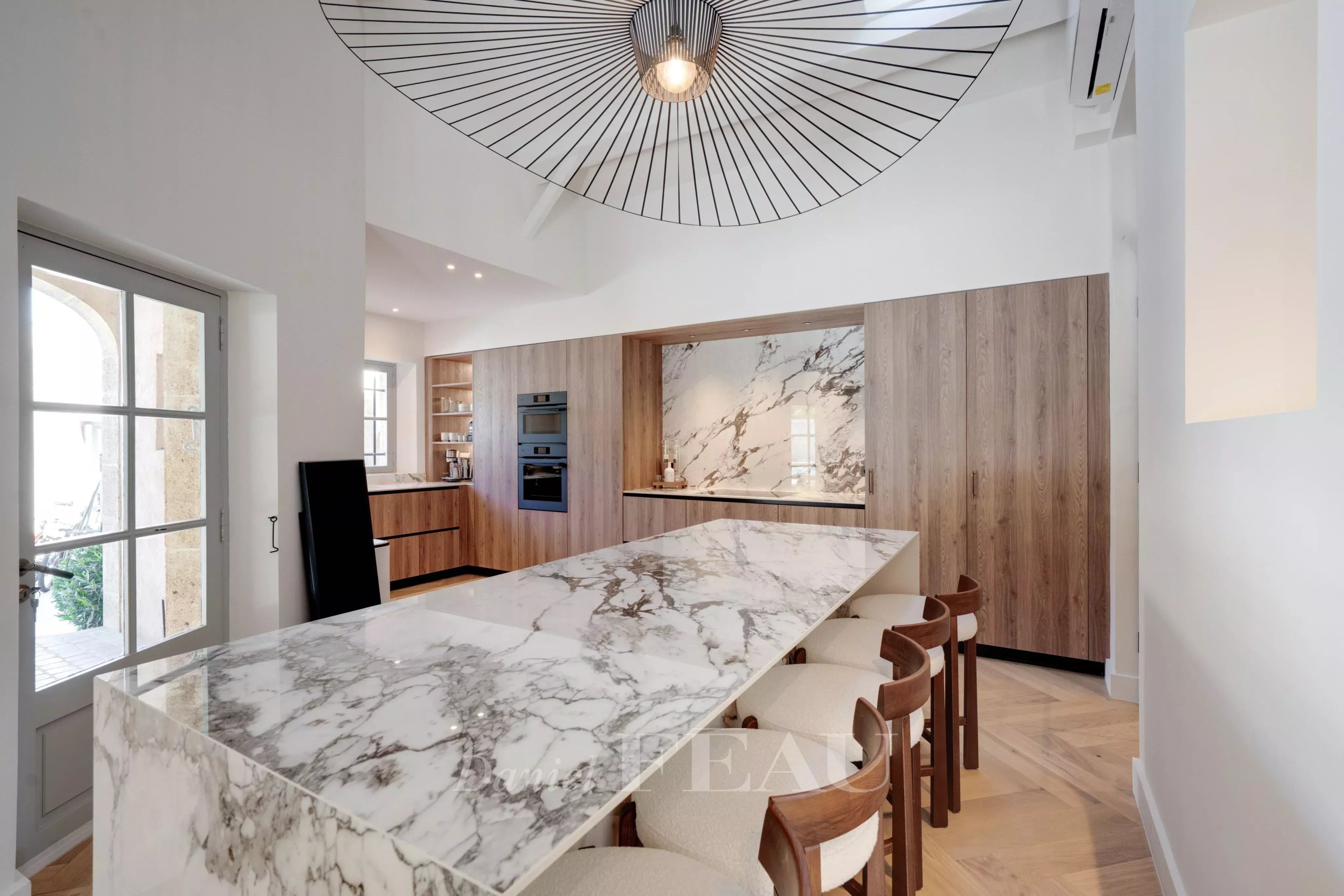 Cuisine moderne avec un grand plan de travail en marbre et des meubles en bois, éclairage design.