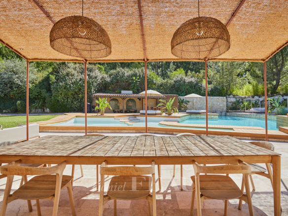 Terrasse en bois avec table et chaises, vue sur piscine et jardin paysager.