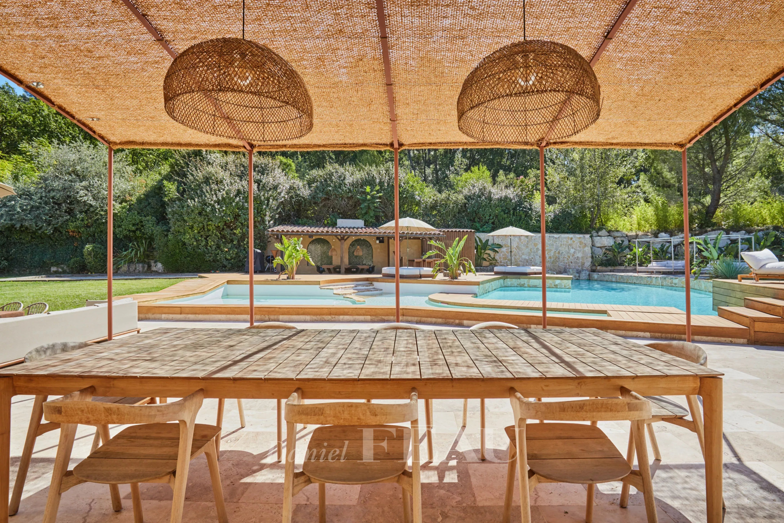 Terrasse en bois avec table et chaises, vue sur piscine et jardin paysager.
