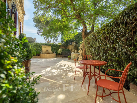 Terrace of an old stone presbytery with red chairs and a fountain, surrounded by greenery.