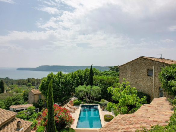 Panoramic view of a stone house with a swimming pool, surrounded by greenery and natural landscapes.