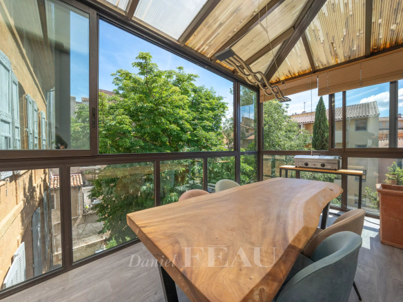 Terrasse vitrée d'un appartement à Aix-en-Provence avec vue sur des arbres et mobilier en bois.