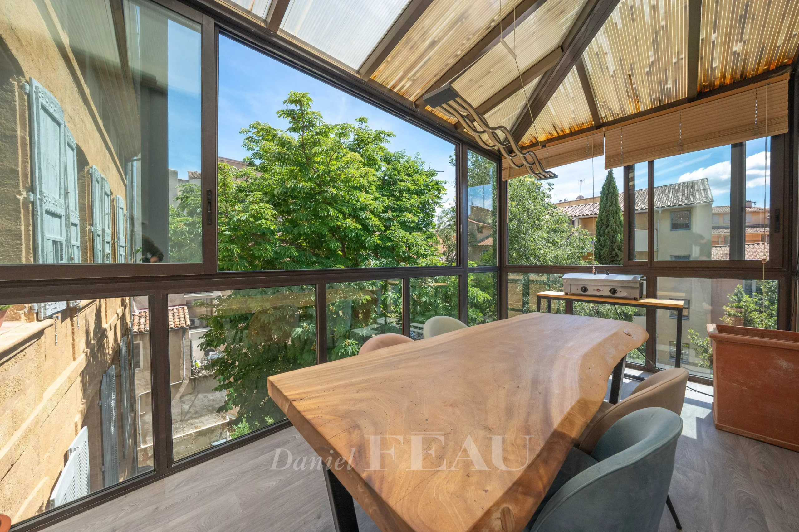 Terrasse d’appartement à Aix-en-Provence Terrasse vitrée d'un appartement à Aix-en-Provence avec vue sur des arbres et mobilier en bois.