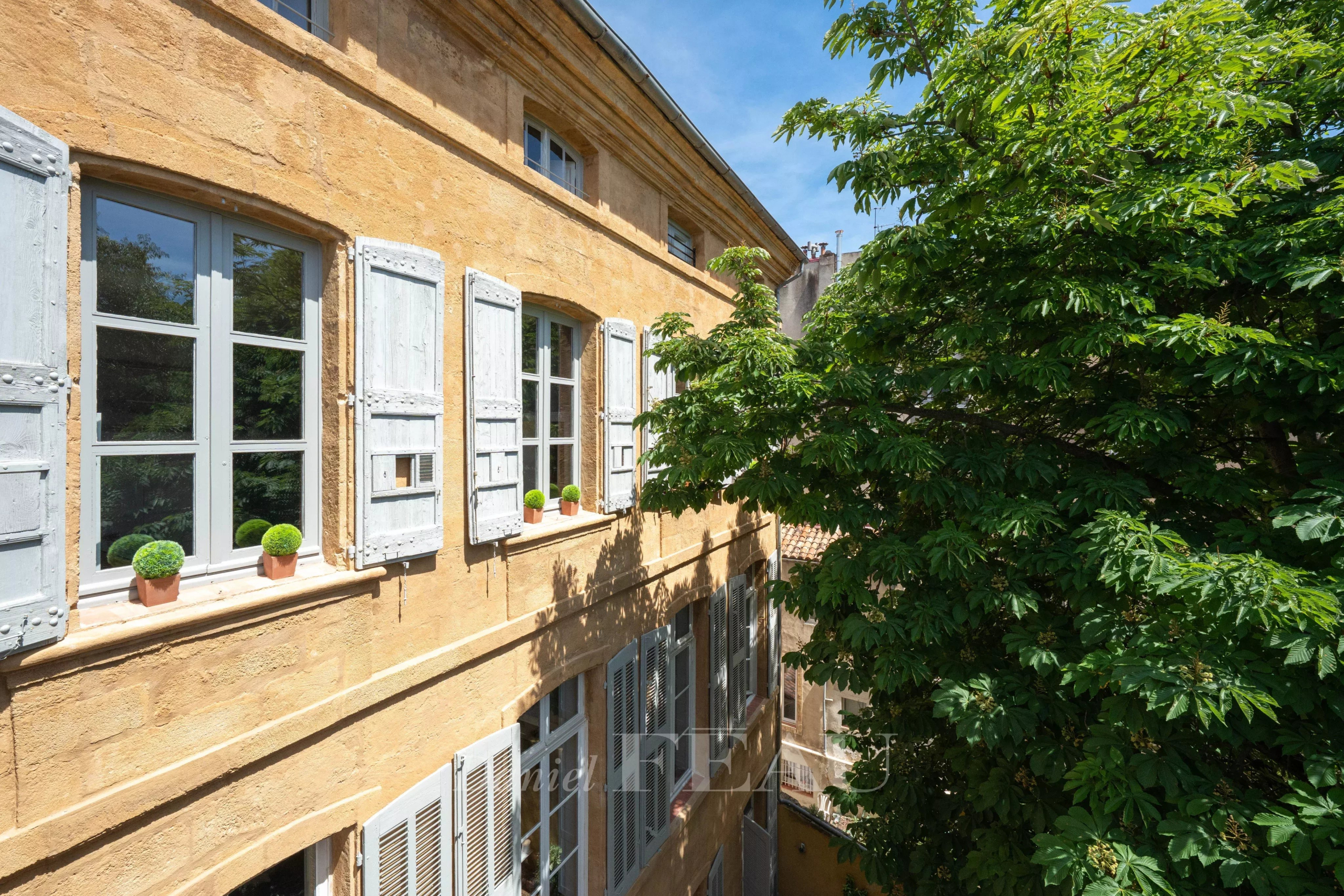Appartement de charme à Aix-en-Provence Façade d'un appartement à Aix-en-Provence avec fenêtres à volets et verdure environnante.