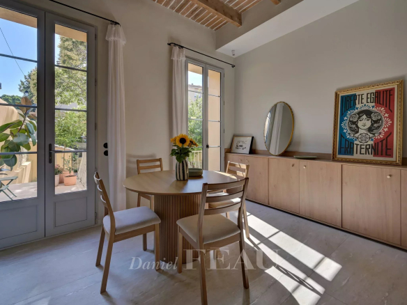 Interior of an apartment in Aix-en-Provence with a round table, chairs and windows opening onto the garden.