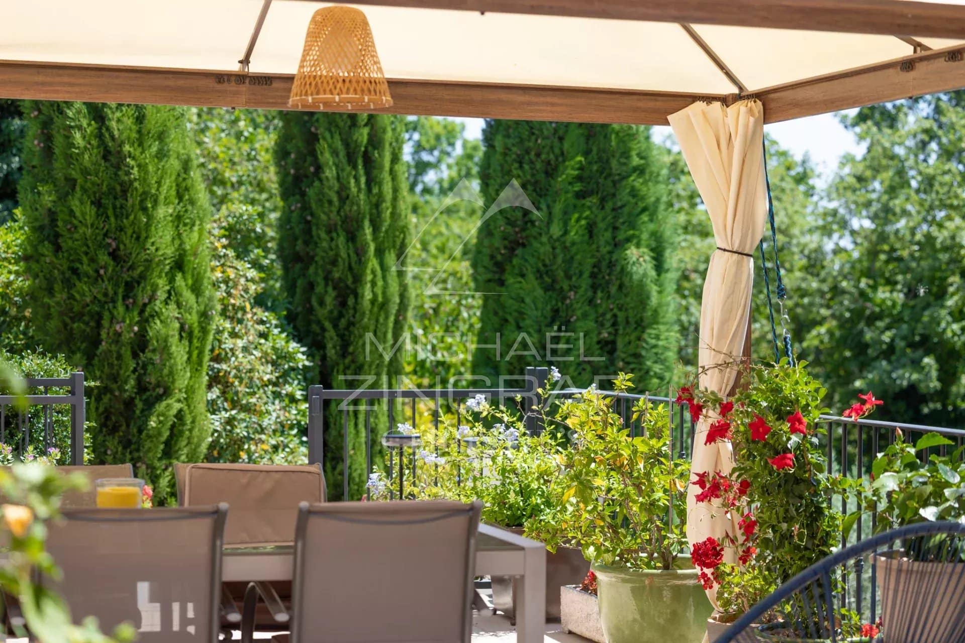 Shaded terrace with garden furniture and flowering plants in a wooded park.