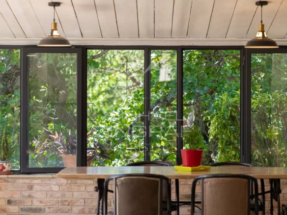 Bright veranda overlooking a wooded park, wooden furniture and plants.