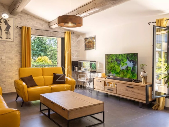 Interior of a bright living room with yellow sofas and a television, windows open onto the garden.